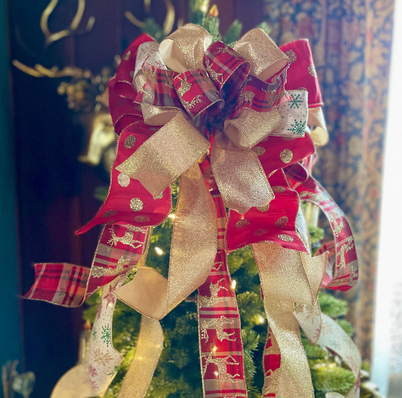 May include: A green Christmas tree decorated with a large gold and red bow, gold and red plaid ribbon, and white ribbon with snowflakes. The tree is also decorated with white lights.