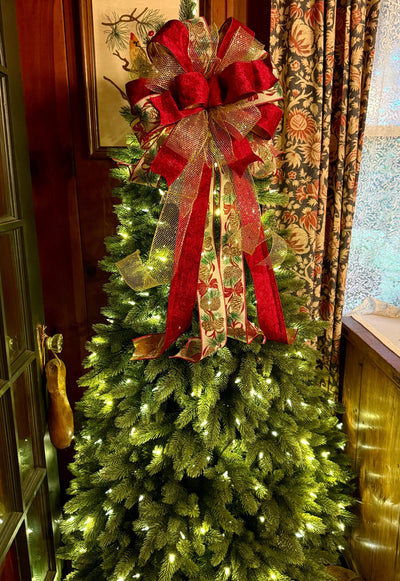 May include: A large decorative Christmas tree topper bow featuring deep red velvet ribbon, gold metallic mesh ribbon, and a cream-colored ribbon printed with a pattern of brown pinecones and green pine needles, with long cascading ribbon tails.